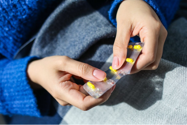 Hands holding a blister pack of yellow capsules against a gray and blue background.