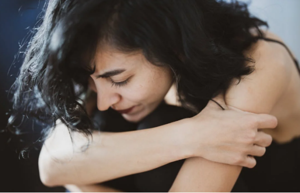 Woman in a black camisole hugging her knees while crying